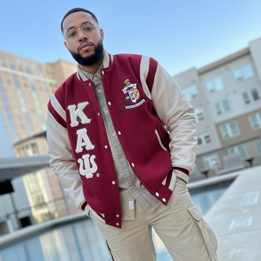 Man wearing a red and beige letterman jacket with 'KAUS' on it, standing outdoors.