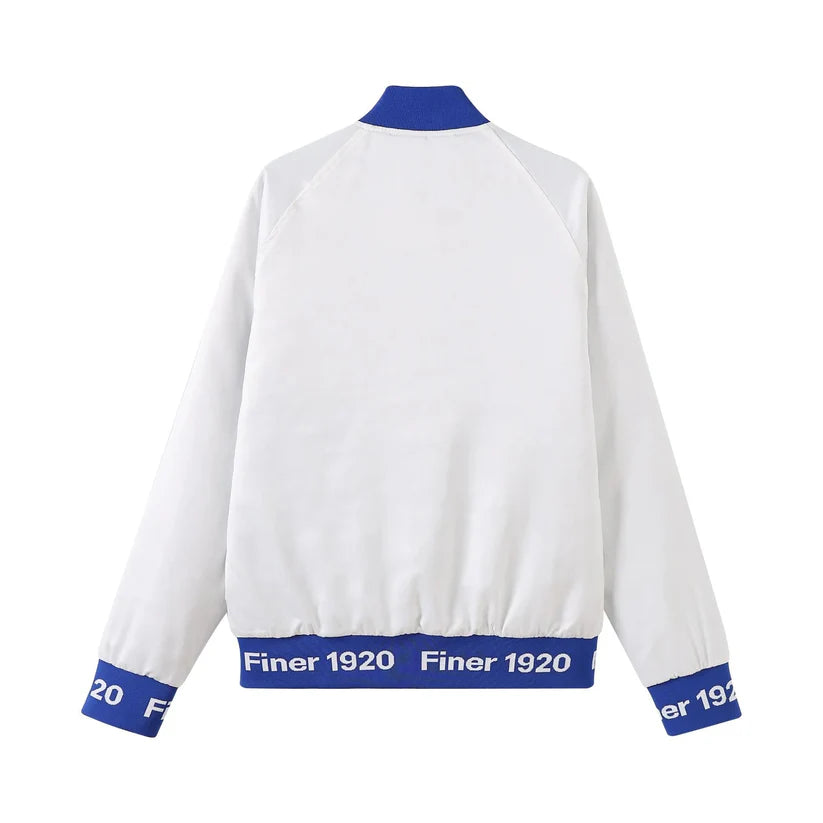 A close-up of the Zeta White Satin Bomber Jacket, highlighting the smooth, glossy satin material and the contrasting Royal Blue custom ribbing and buttons. Shows the embroidered Zeta logo and the quality details.